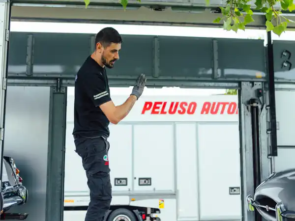 Uomo con t-shirt nera e guanti che indica e coordina il carico di un veicolo all’interno di un camion Peluso Automotive