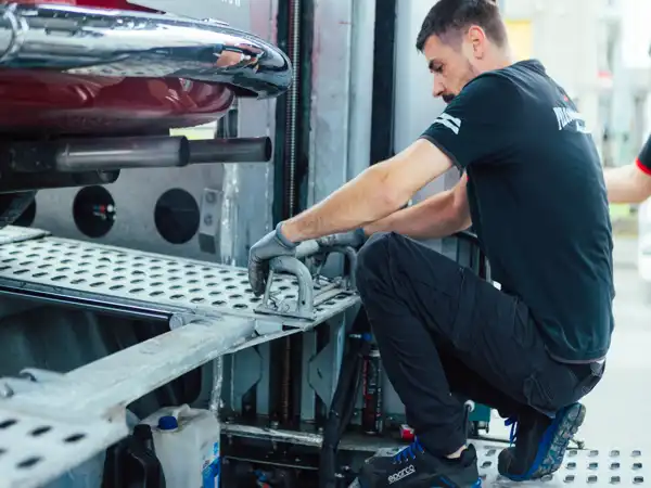 Tecnico con guanti che esegue manutenzione su una piattaforma metallica di trasporto veicoli