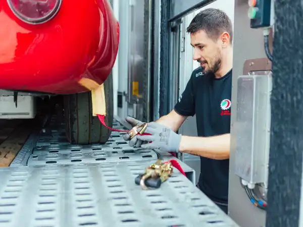 Tecnico con guanti che assicura un'auto d'epoca con una cinghia rossa su un carrello metallico di un camion di trasporto veicoli